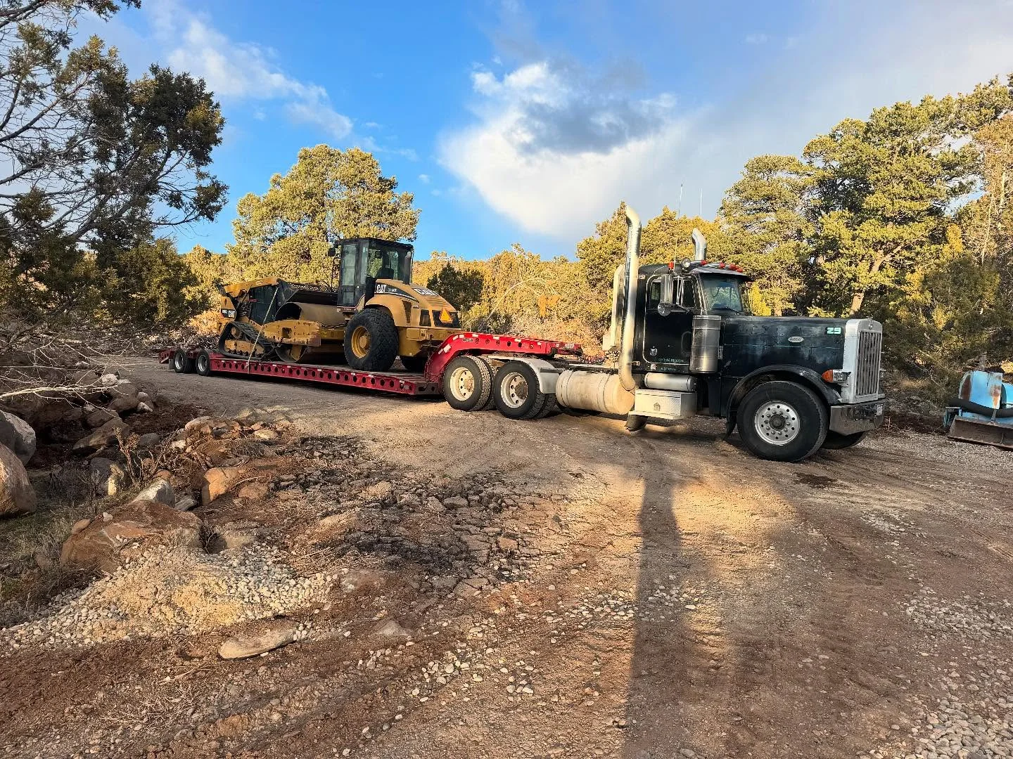 Truck and lowboy trailer carrying a tracked loader to a wooded job site