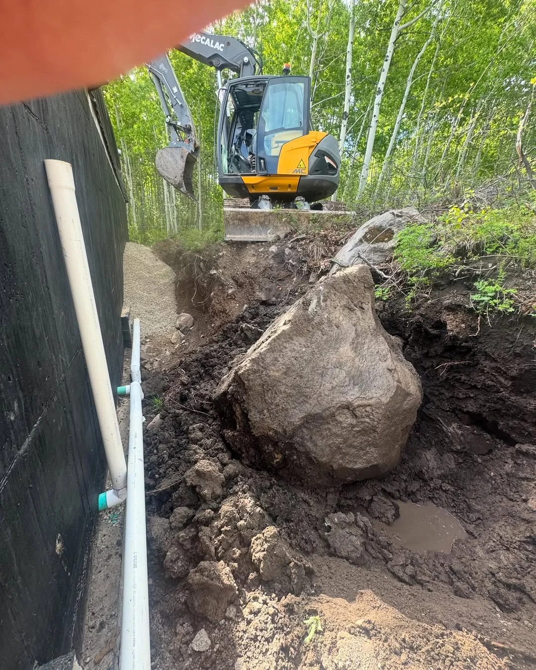 Large exposed boulder beside an excavator at a residential work site