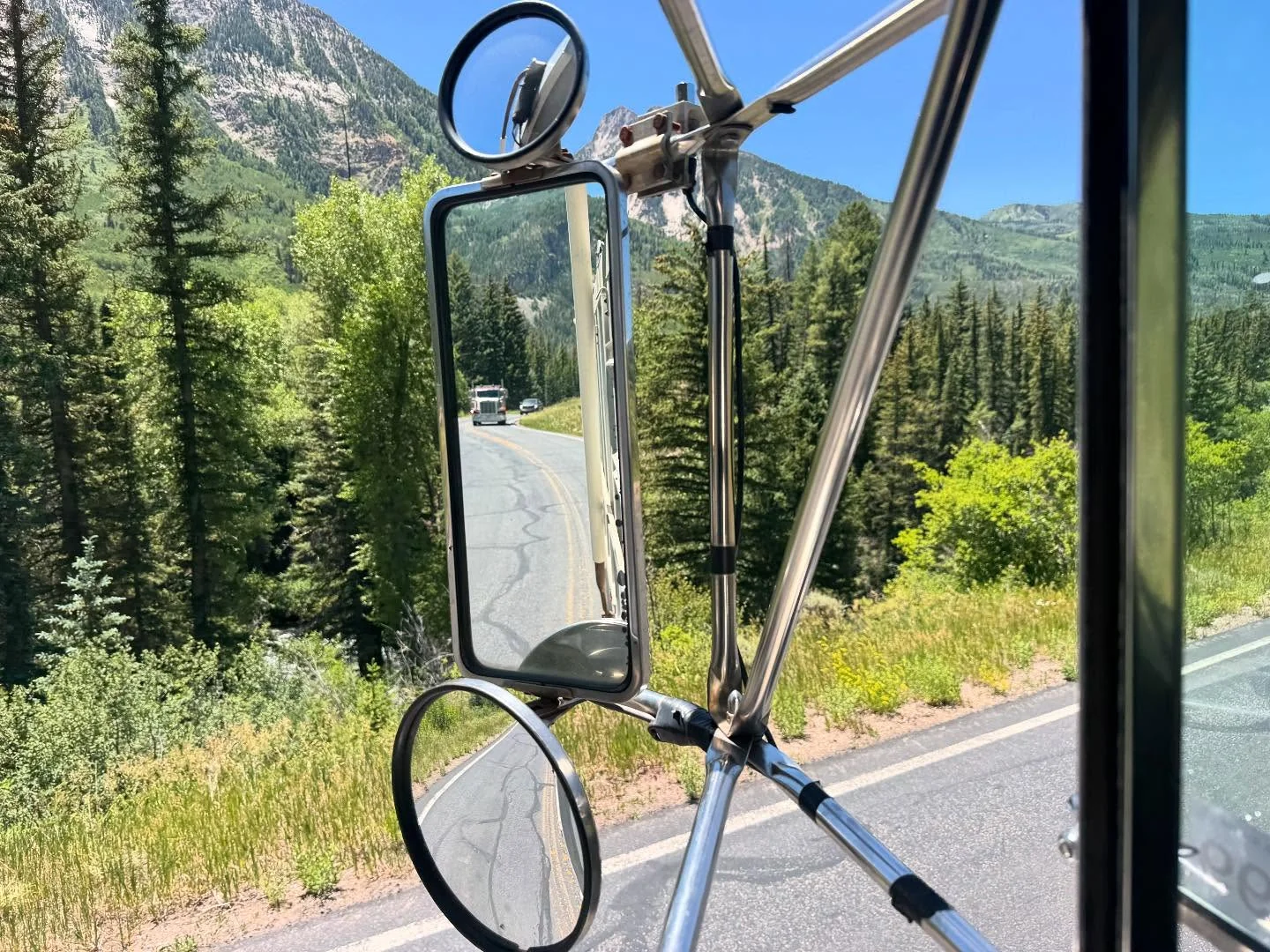 Truck mirrors reflecting a trailer along a tree-lined road
