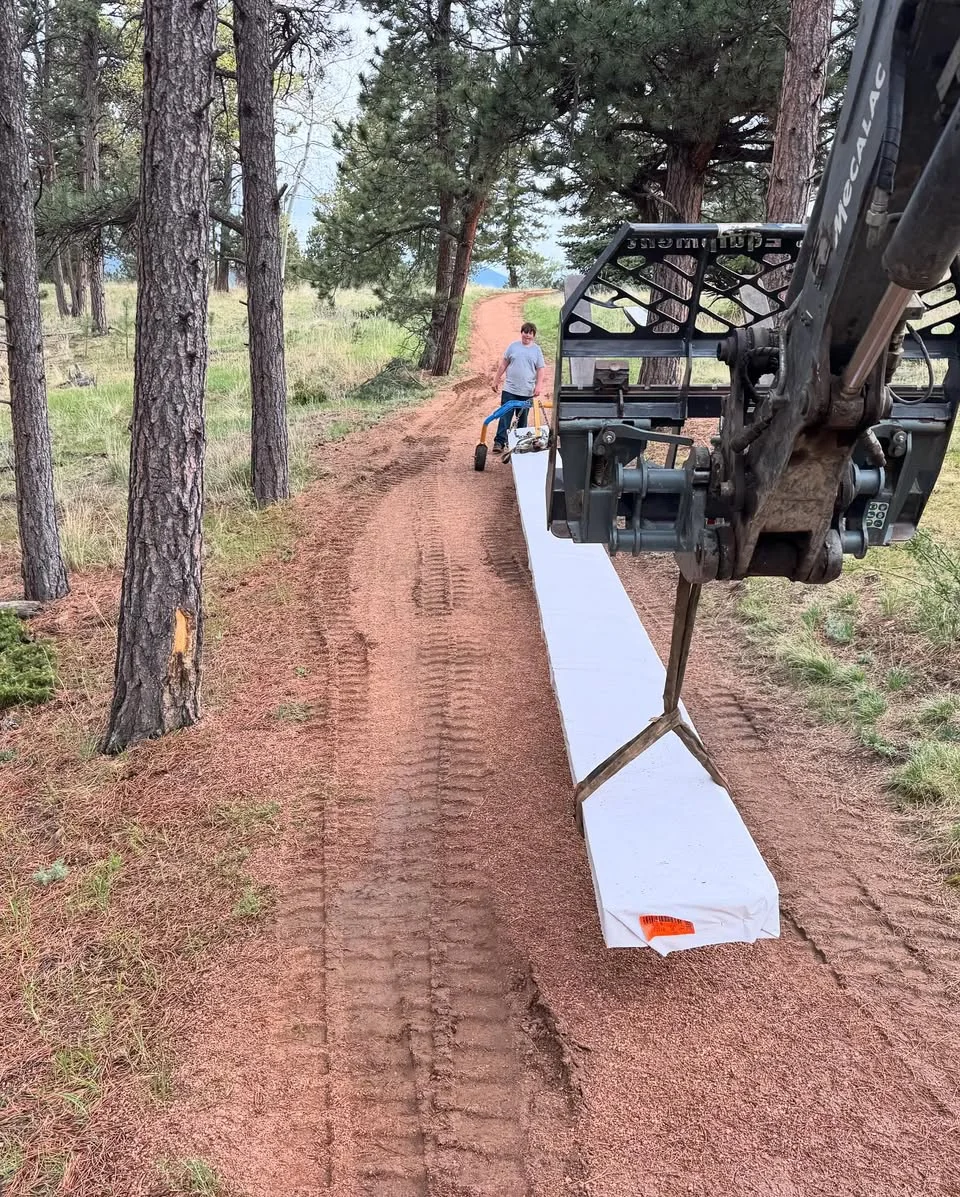 Graded dirt access route through trees seen beside an excavator attachment